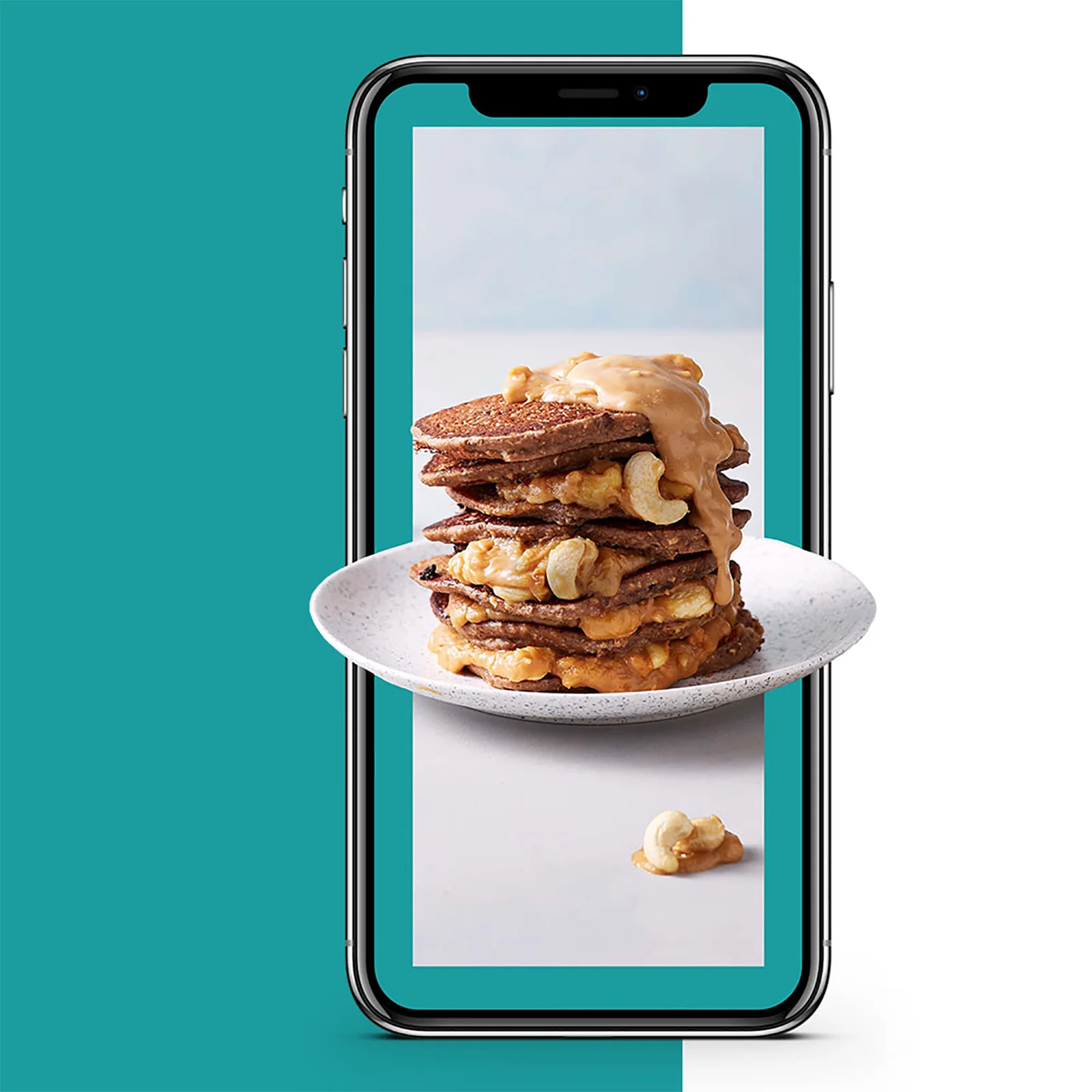 Foto van een telefoon met een stapel pannenkoeken met saus en cashewnoten op het scherm.