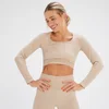 Een vrouw draagt een crèmekleurige, geribbelde, naadloze croptop met lange mouwen en bijpassende legging.