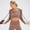 Een vrouw draagt een hazelnootbruine, naadloze croptop met lange mouwen en bijpassende legging.