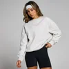 Een vrouw draagt een lichtgrijze, oversized sweatshirt met lange mouwen en zwarte sportshorts.