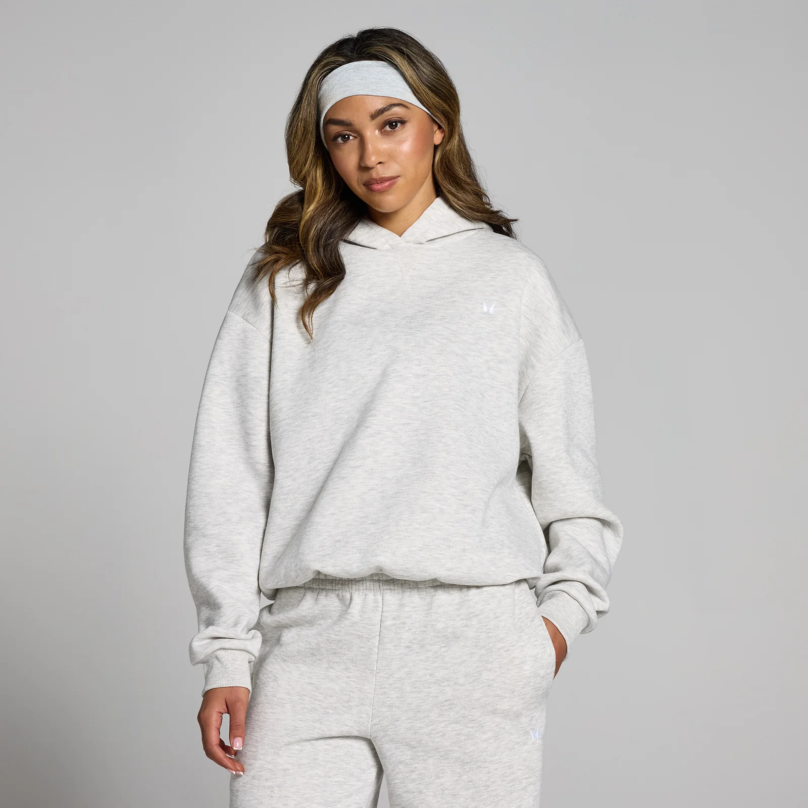 Een vrouw draagt een gemêleerd lichtgrijze oversized hoodie met capuchon en bijpassende joggingbroek.