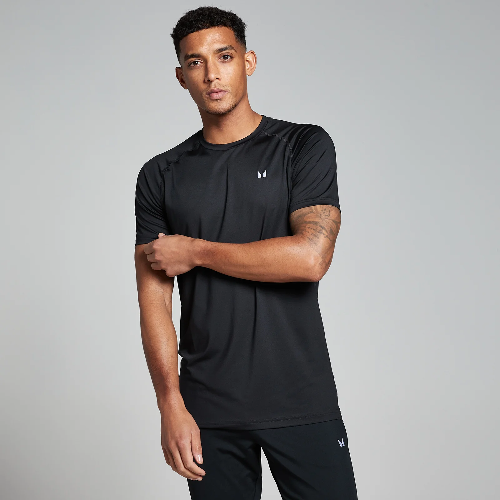 Een man draagt een zwart trainingsshirt met korte mouwen en een klein wit logo.