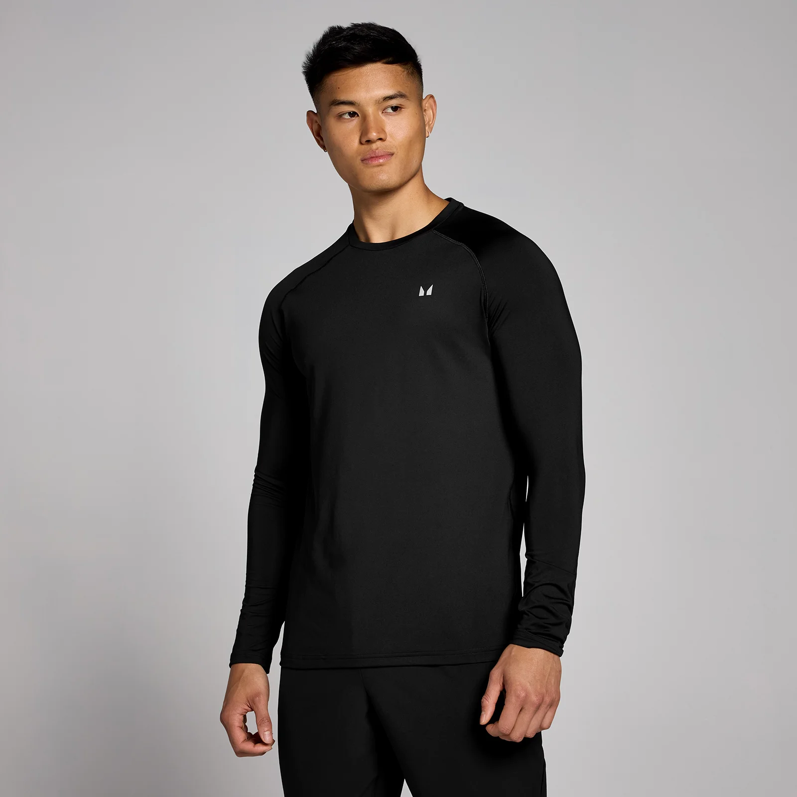 Een man draagt een zwart trainingsshirt met lange mouwen en een klein wit logo.