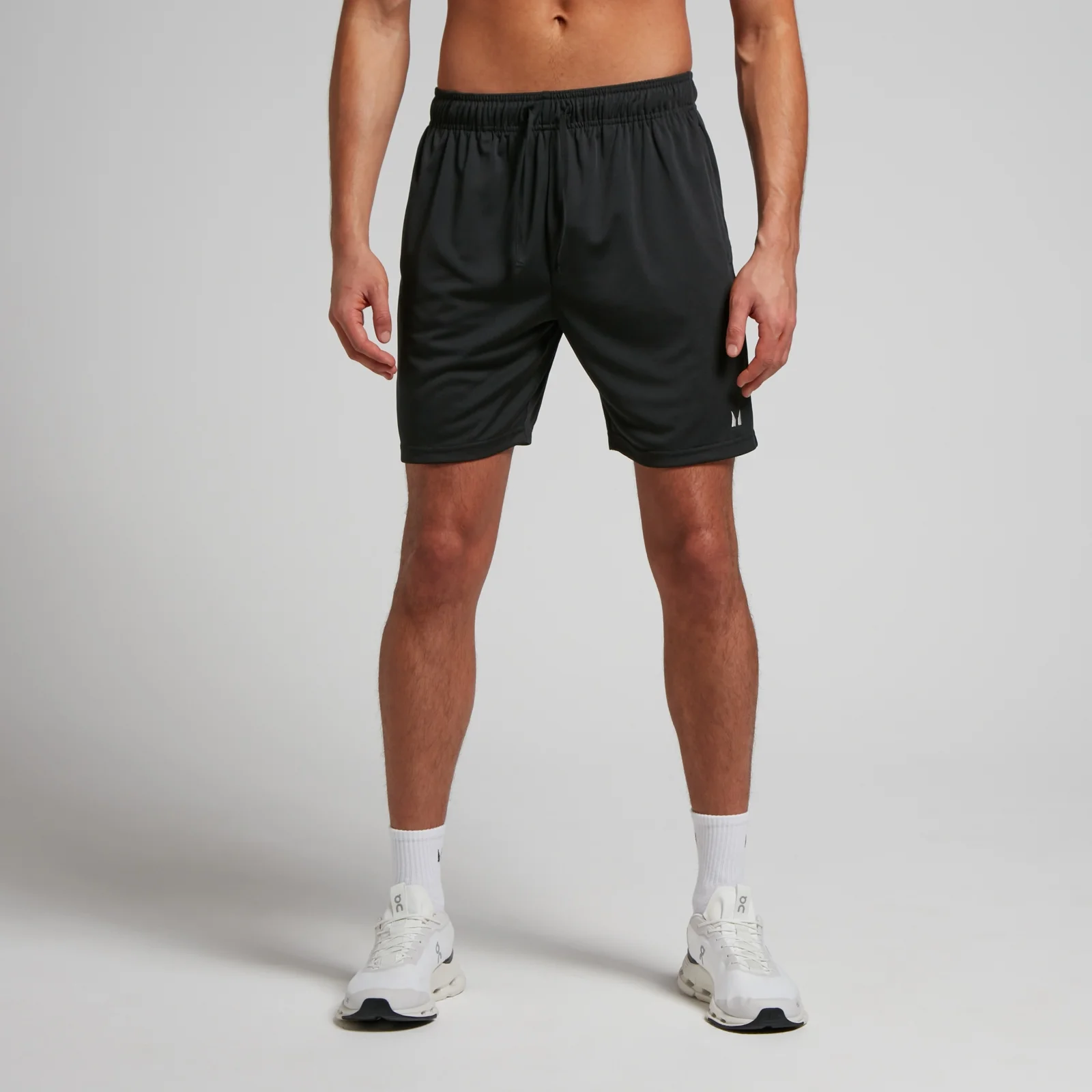 Een man draagt een zwarte, korte sportbroek met een elastische tailleband en witte sportschoenen.