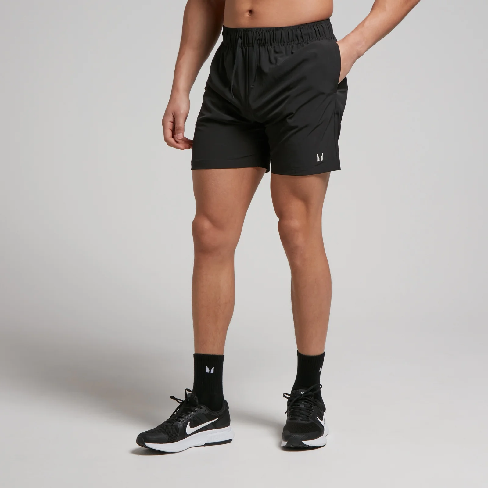 Een man draagt een zwarte, geweven trainingsshort met een elastische tailleband en het MP-logo.