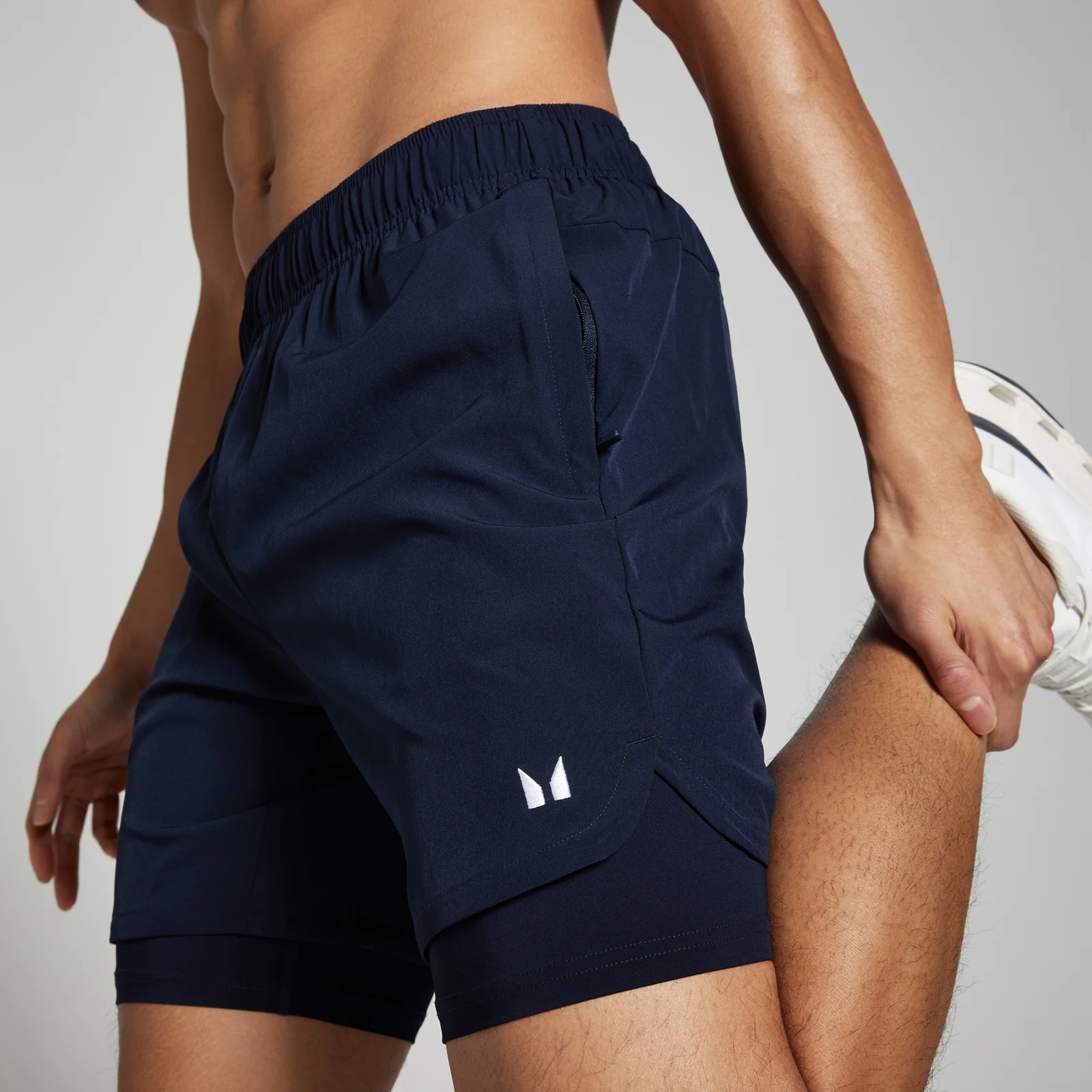 Een marineblauwe 2-in-1 trainingsshort voor heren met een elastische tailleband en een wit logo.