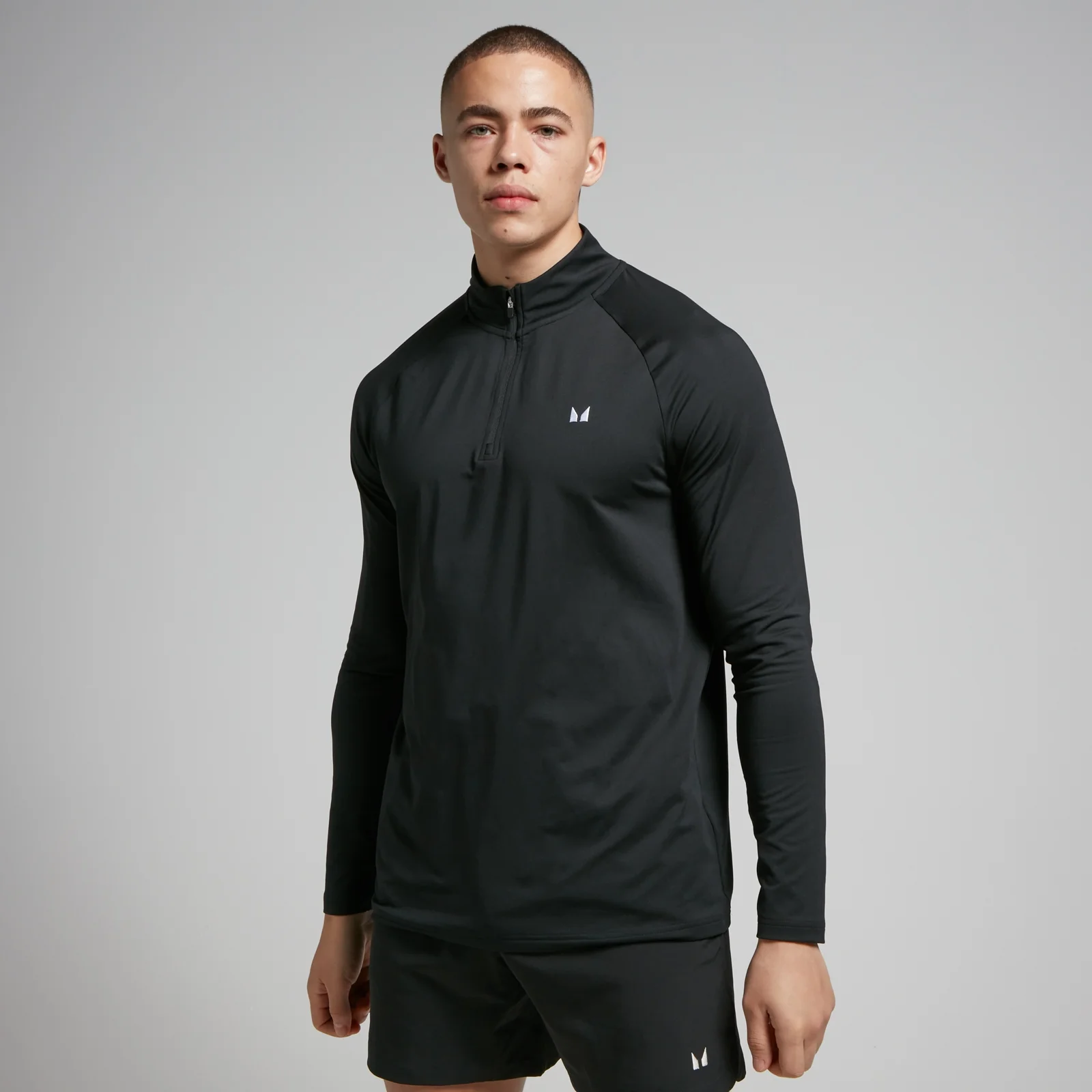 Een man draagt een zwarte trainingsoutfit met lange mouwen en een korte broek.