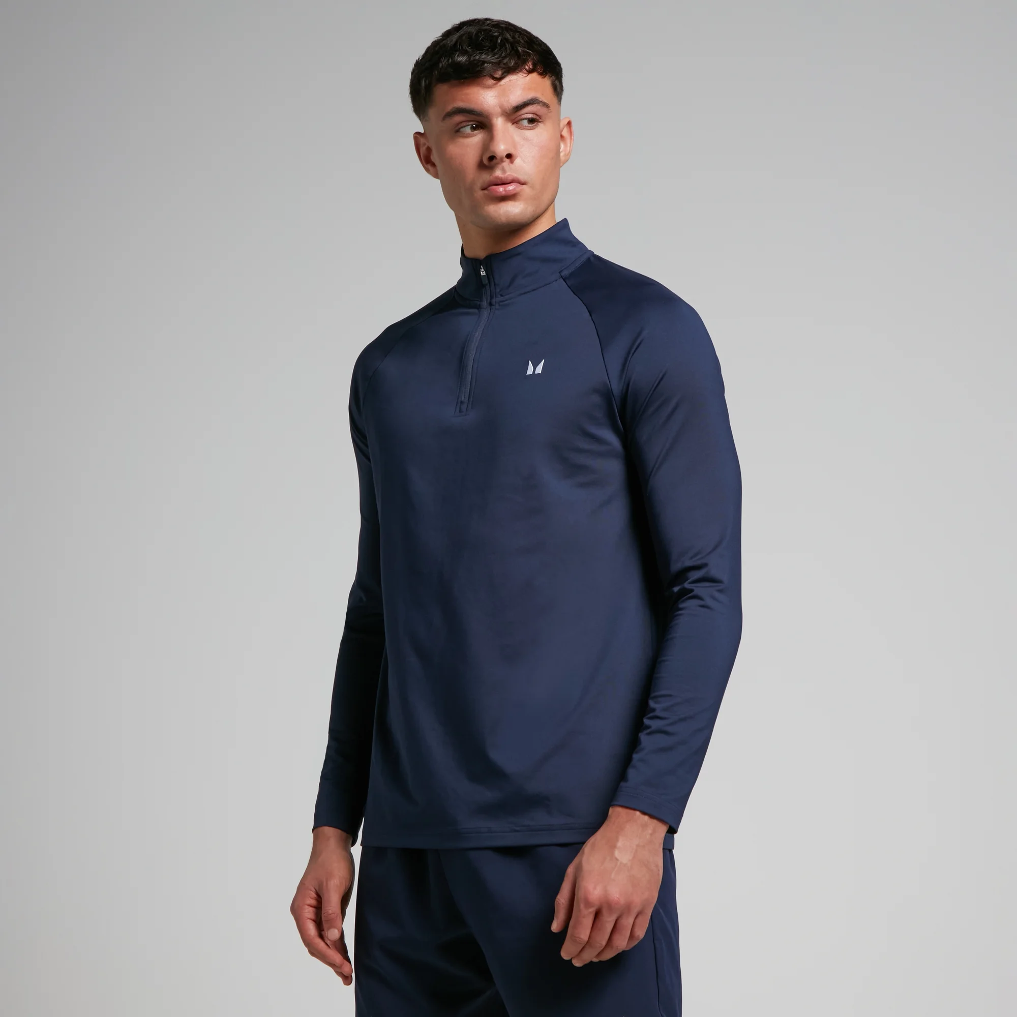Een marineblauw trainingspak met lange mouwen en een korte rits, met een klein logo.