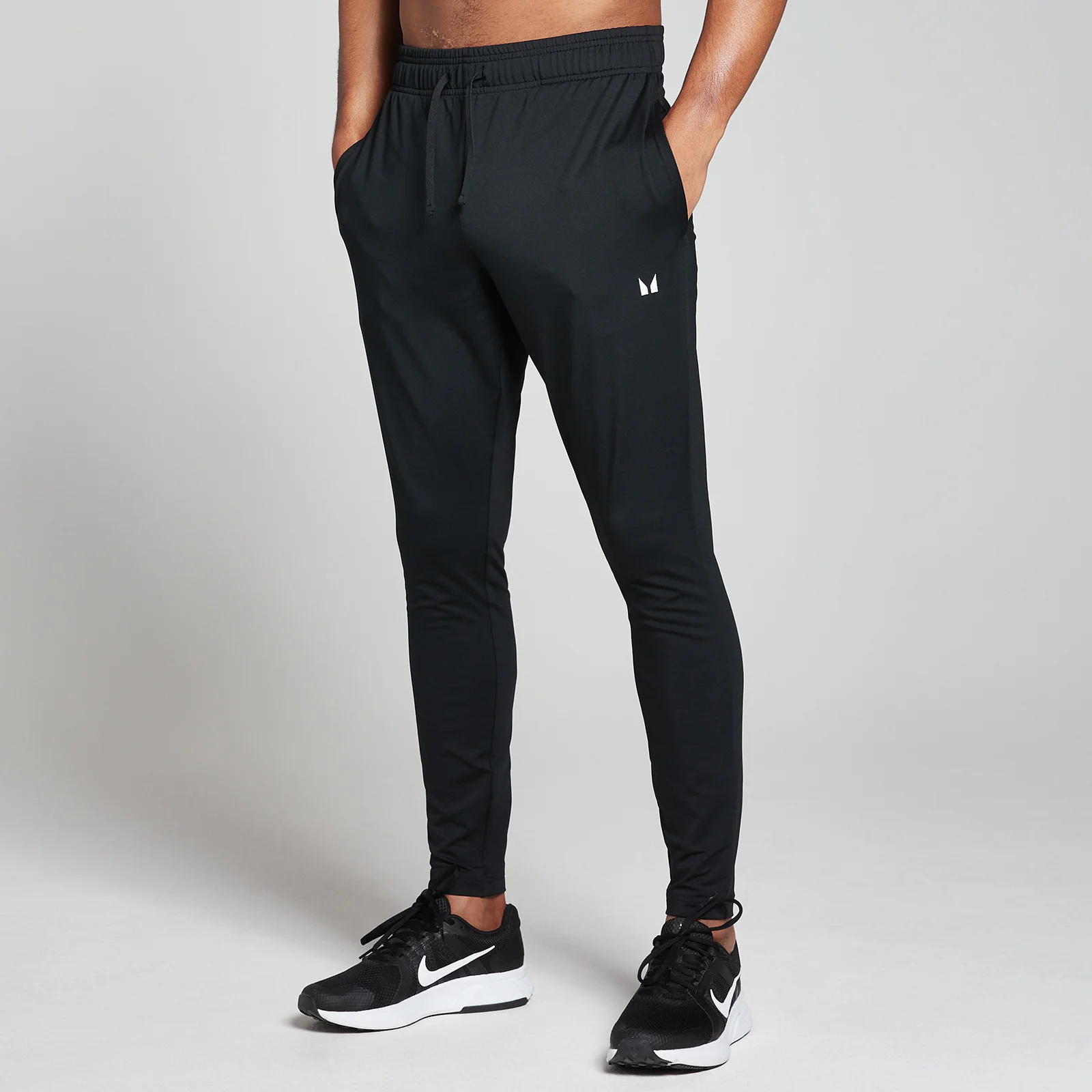 Een zwarte trainingsbroek met trekkoord en het MP logo, gedragen met zwarte sportschoenen.