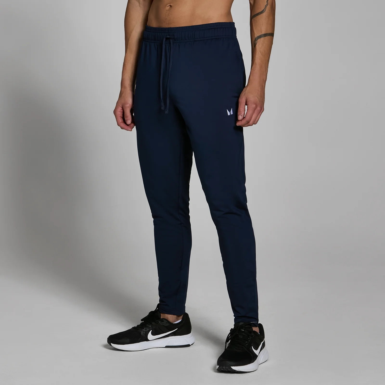 Een marineblauwe trainingsbroek met trekkoord en een klein wit logo op de dij.