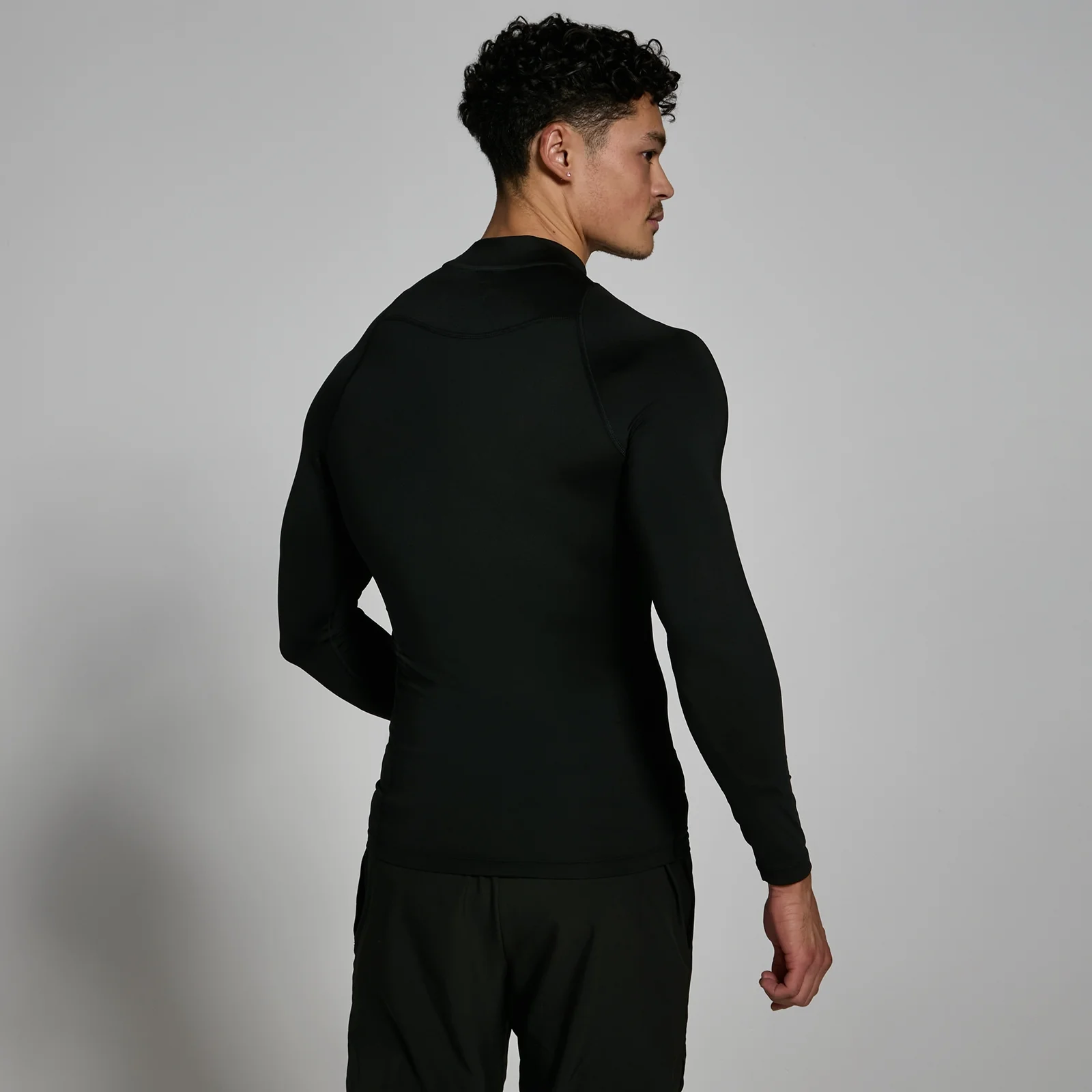 Een man draagt een zwart, nauwsluitend sportshirt met lange mouwen en een hoge hals.