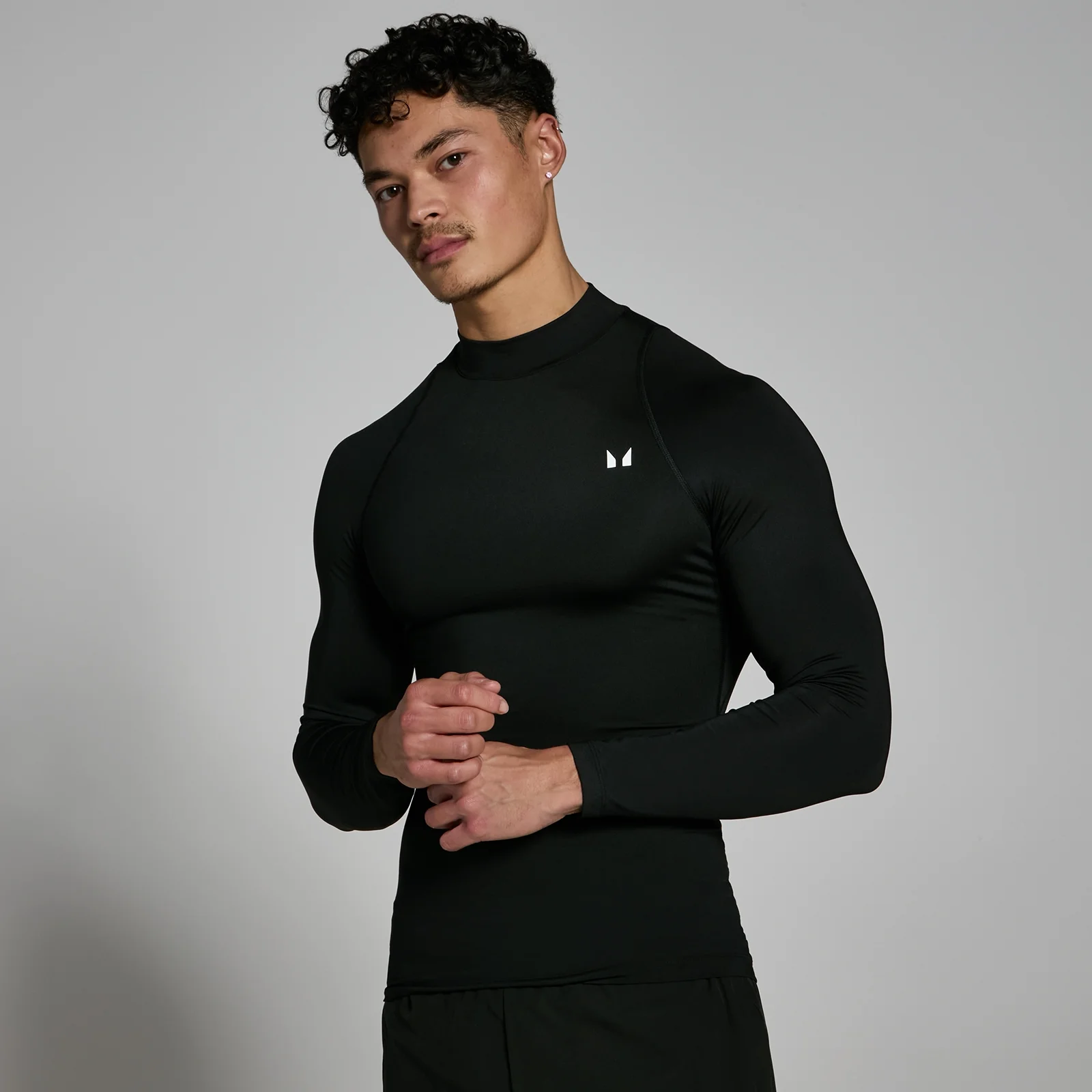 Een man draagt een zwart, aansluitend sportshirt met lange mouwen en een hoge hals.