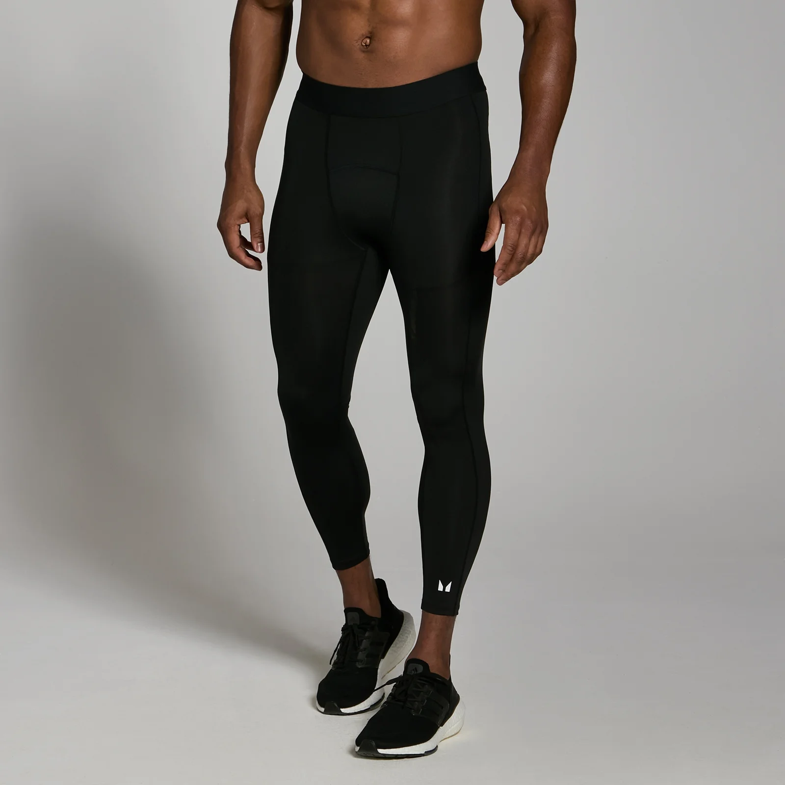 Een man draagt een zwarte, driekwart trainingslegging met een klein wit logo op de kuit.