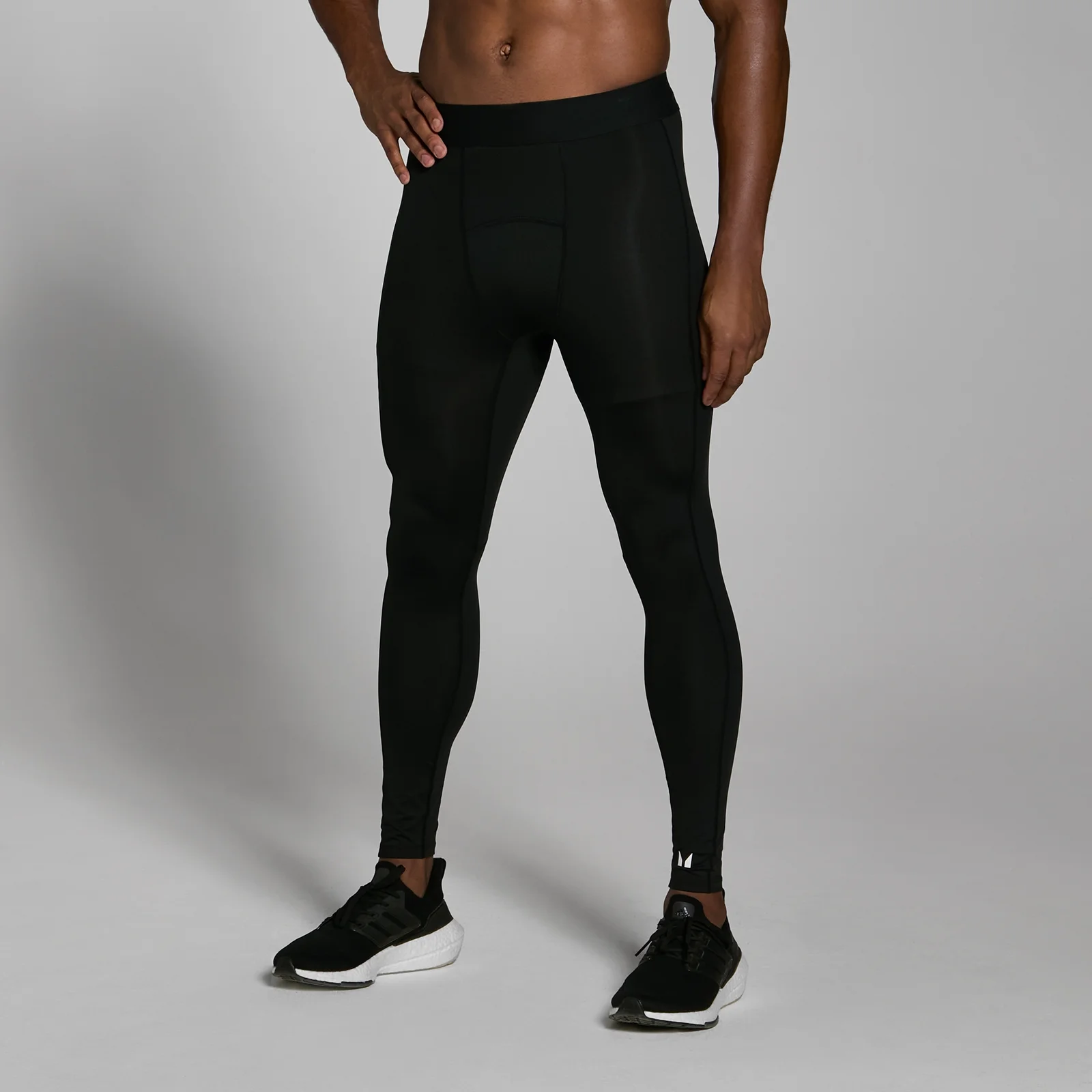 Een man draagt een zwarte, nauwsluitende trainingslegging tot aan de enkels, met zwarte sportschoenen.