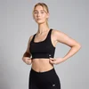 Een vrouw draagt een zwarte, naadloze sportbeha met gekruiste bandjes en een klein wit logo.