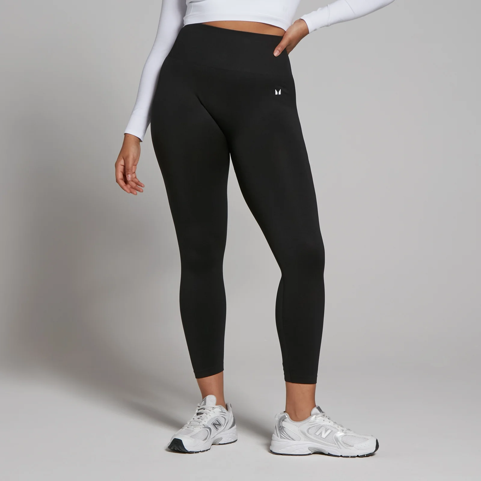 Een vrouw draagt een zwarte, naadloze 7/8 legging met een hoge taille en een klein logo.