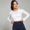 Een vrouw draagt een witte, naadloze croptop met lange mouwen en een klein logo.