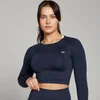 Een vrouw draagt een marineblauwe, naadloze croptop met lange mouwen en een wit logo.