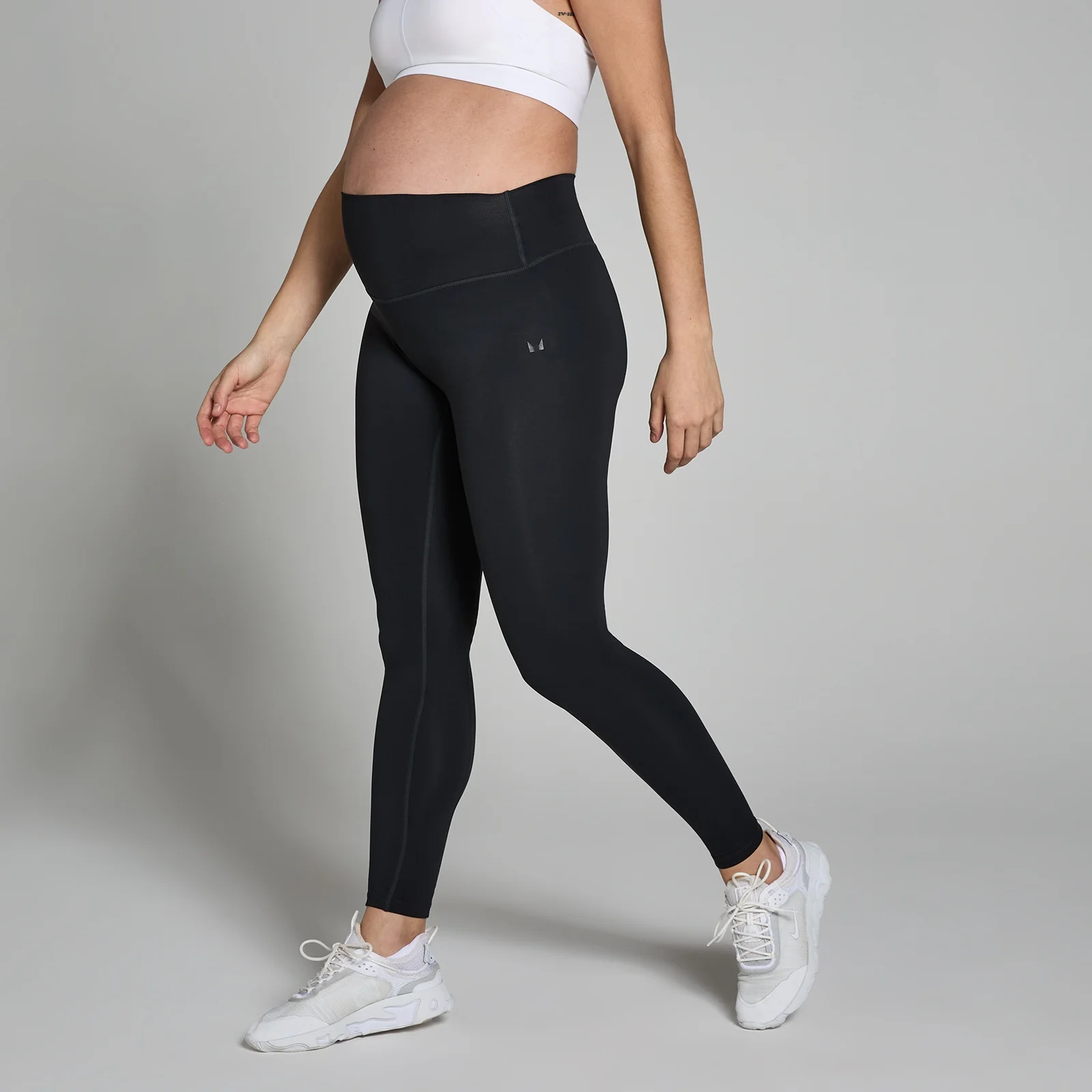Een zwangere vrouw draagt een zwarte, middelhoge zwangerschapslegging en witte sportschoenen.