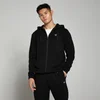 Een man draagt een zwarte hoodie met rits en een klein wit logo, met bijpassende zwarte broek.