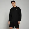 Een man draagt een zwarte sweatshirt met een klein wit logo en zwarte shorts.