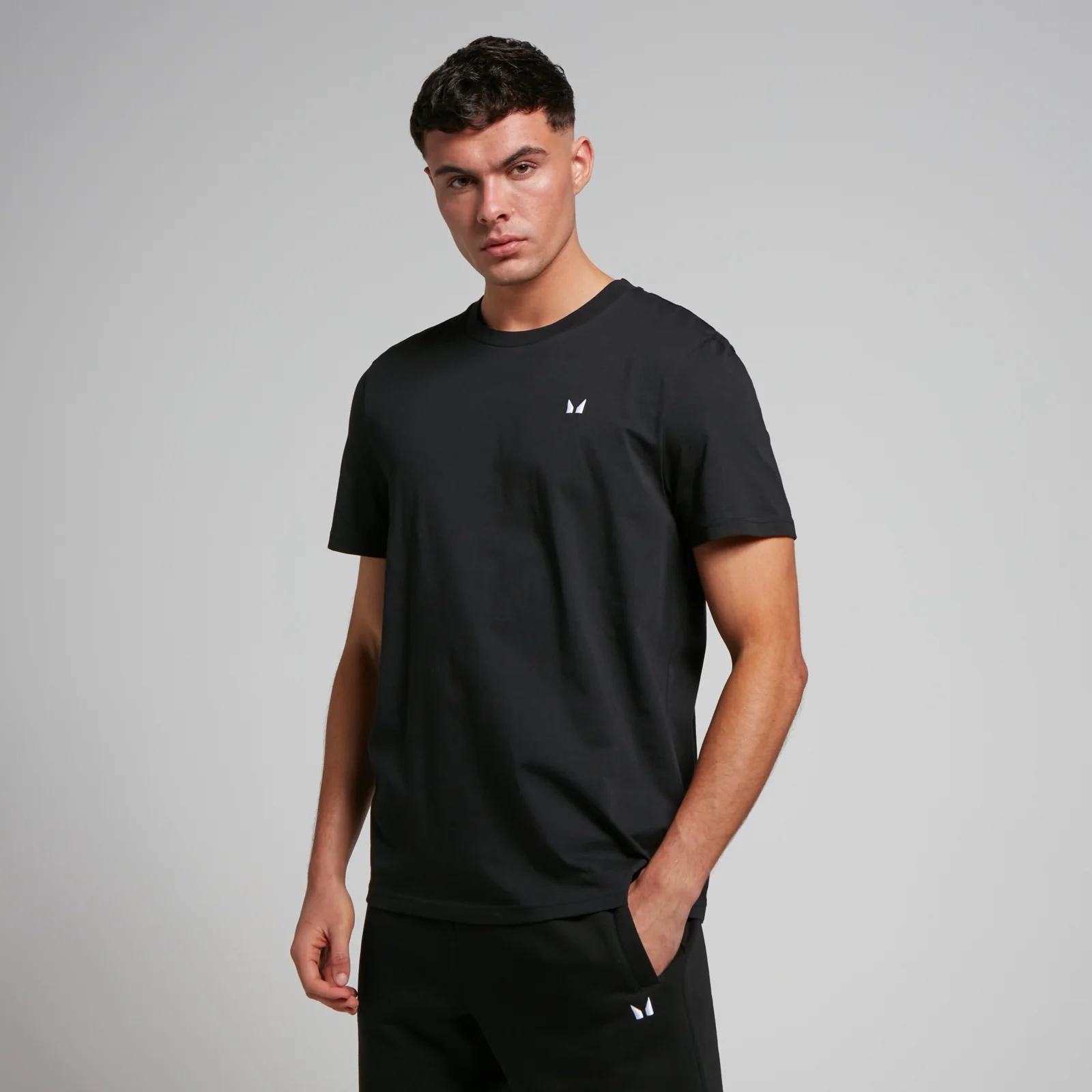 Een man draagt een zwart T-shirt met korte mouwen en een klein wit logo.