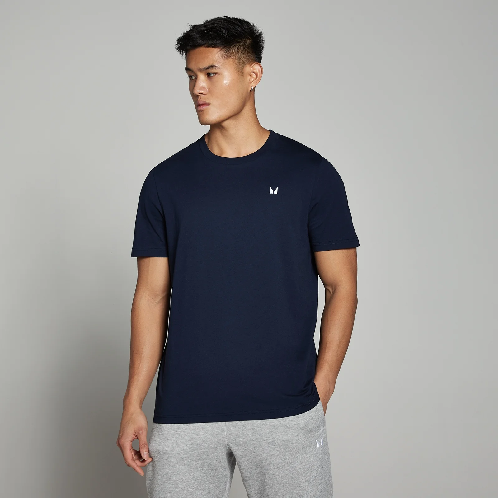 Een man draagt een marineblauw T-shirt met korte mouwen en een klein wit logo.