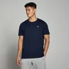 Een man draagt een marineblauw T-shirt met korte mouwen en een klein wit logo.