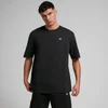 Een man draagt een zwart, oversized T-shirt met korte mouwen en een klein wit logo.