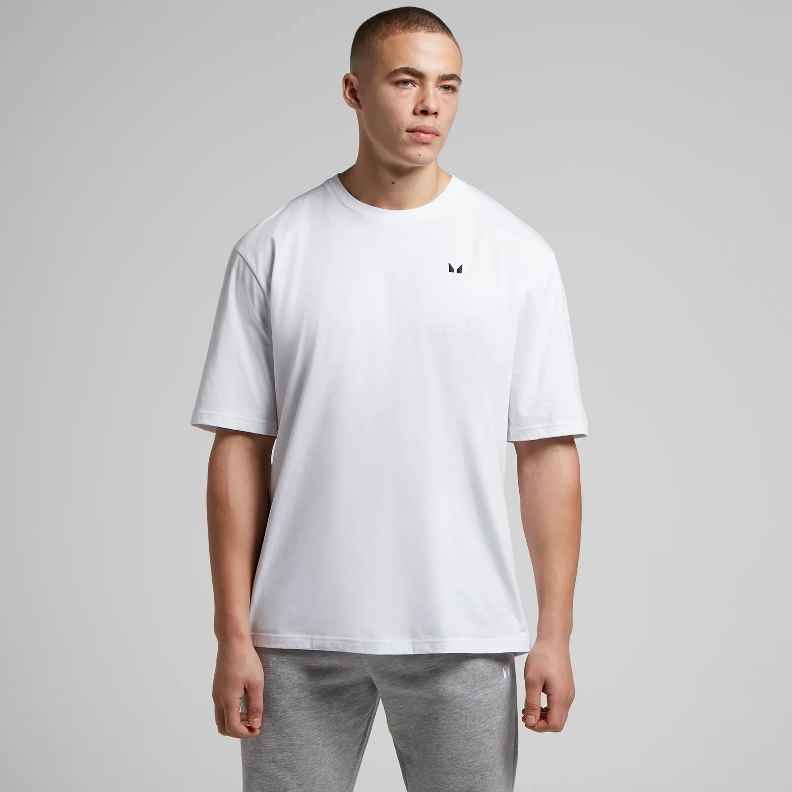 Een man draagt een wit, oversized T-shirt met een klein, donker logo.