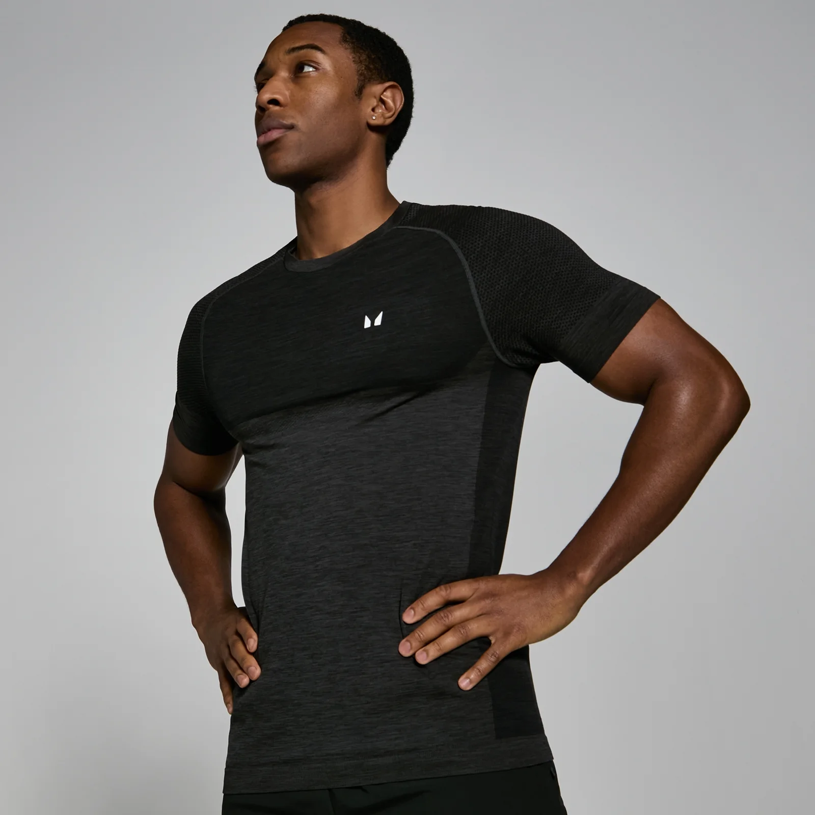Een man draagt een zwart gemêleerd T-shirt met korte mouwen en een klein wit logo.