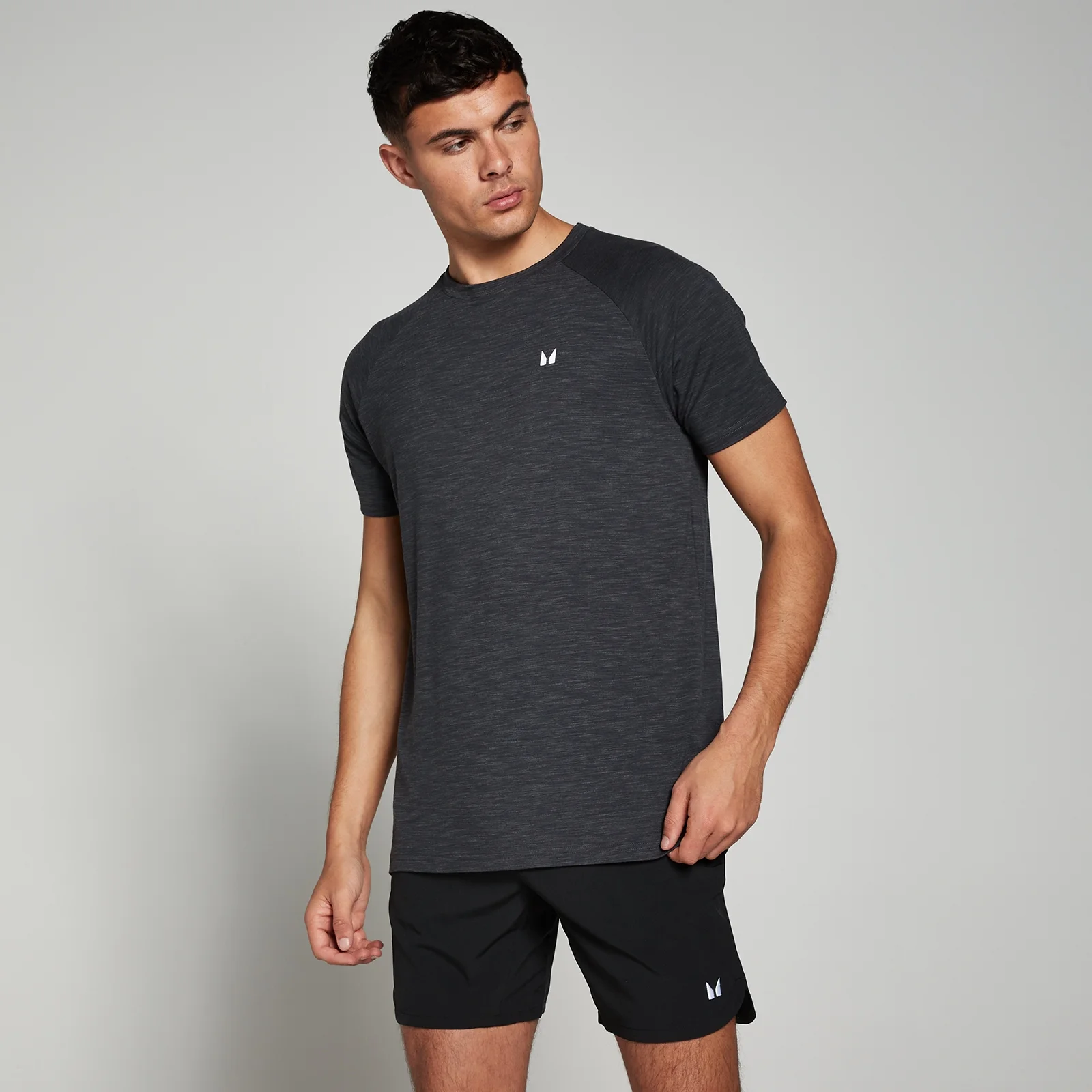 Een man draagt een gemêleerd zwart T-shirt met korte mouwen en een klein wit logo.