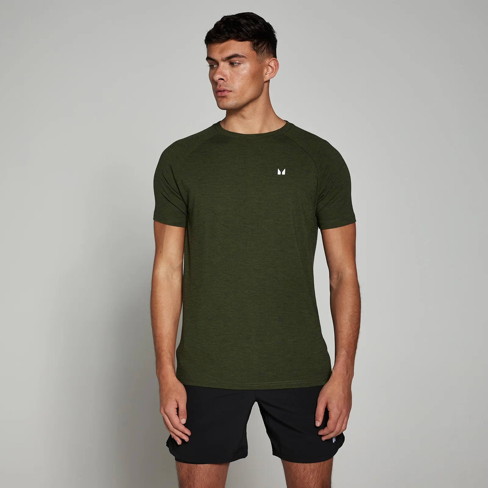 Een man draagt een gemêleerd legergroen T-shirt met korte mouwen en een klein wit logo.