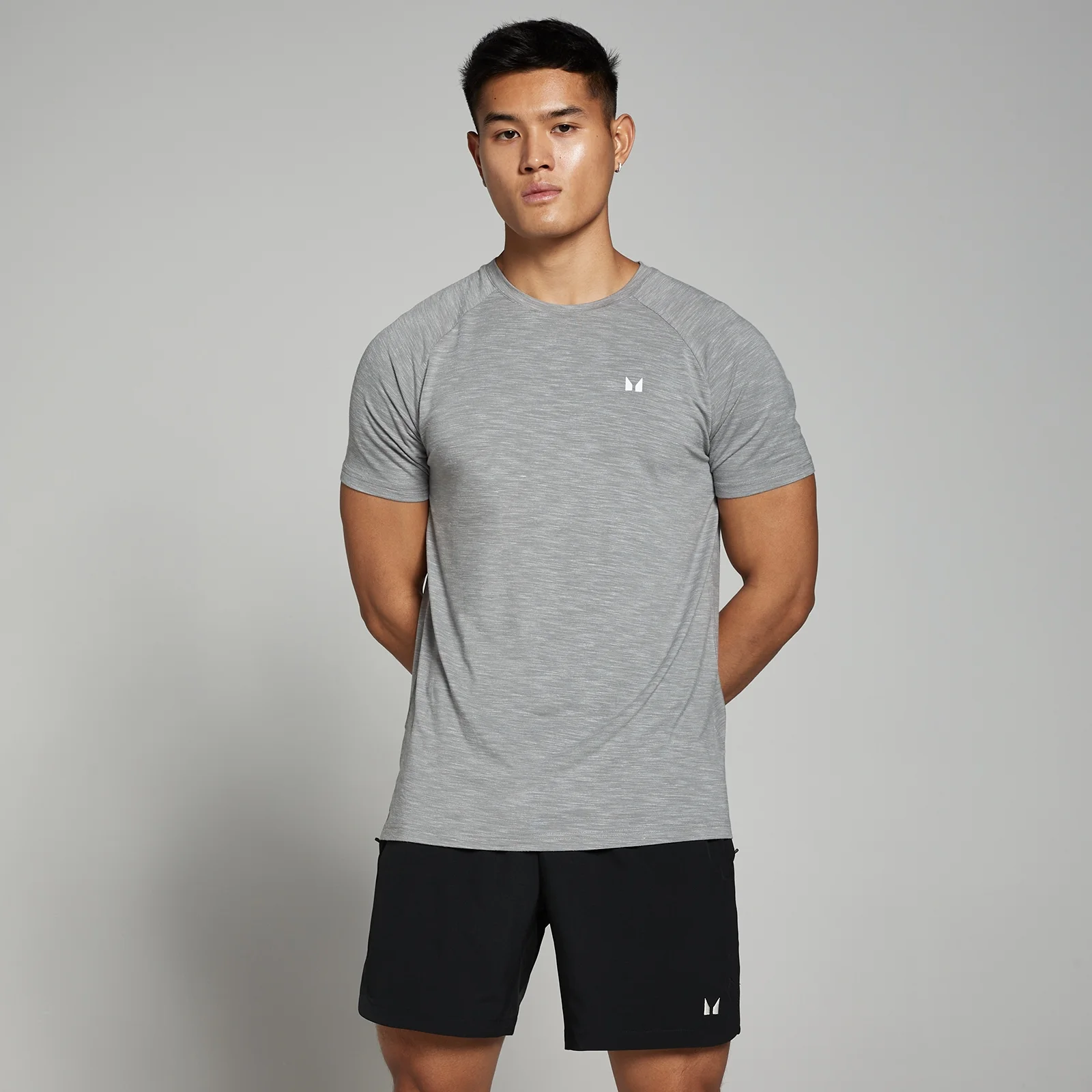 Een man draagt een grijs gemêleerd T-shirt met korte mouwen en zwarte shorts.