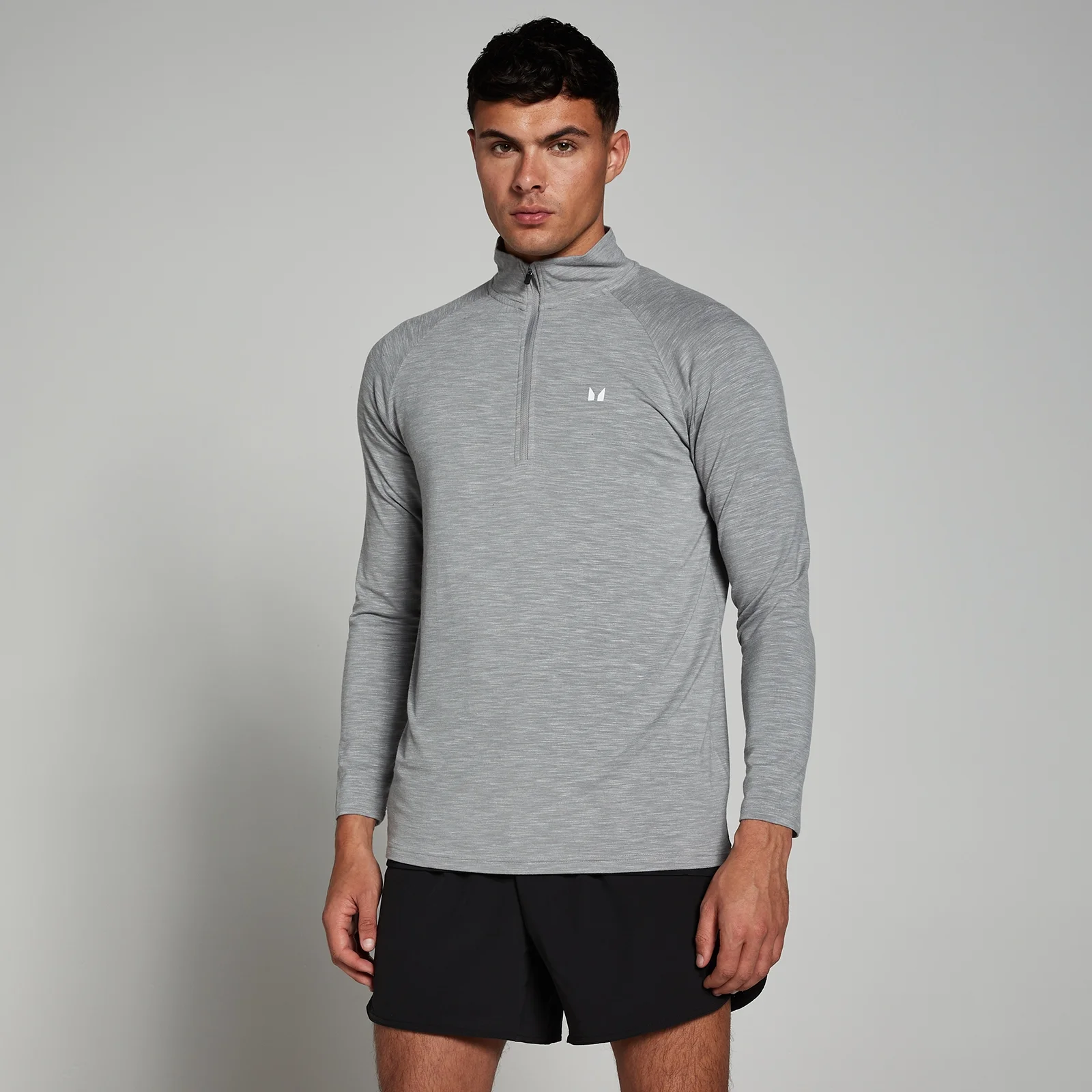 Een man draagt een grijs, gemêleerd sportshirt met lange mouwen en een korte rits.