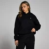 Een vrouw draagt een zwarte, oversized hoodie met een klein wit logo.