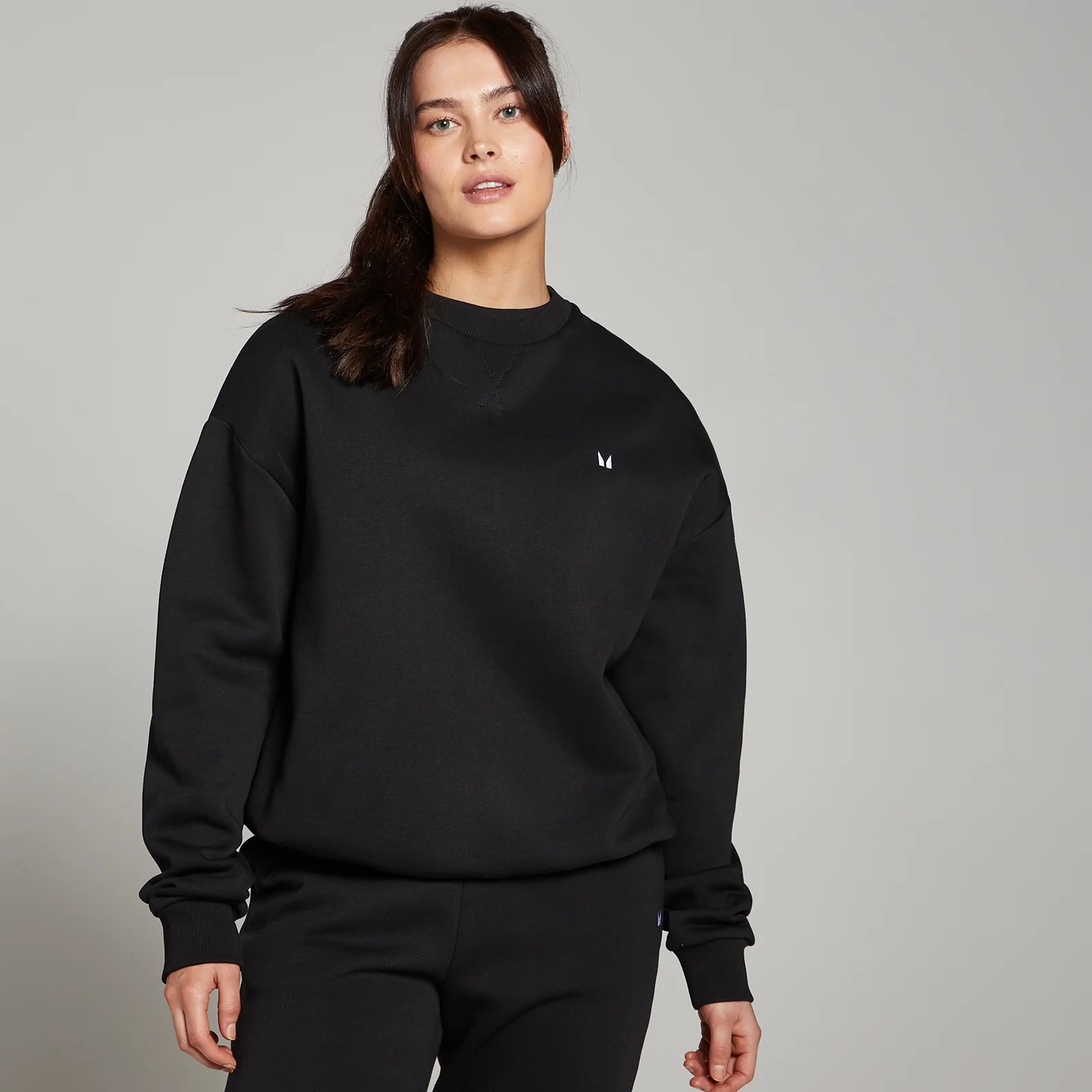 Een vrouw draagt een zwarte, oversized sweatshirt met een klein wit logo.