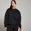 Een vrouw draagt een zwarte, oversized sweatshirt met een klein wit logo.