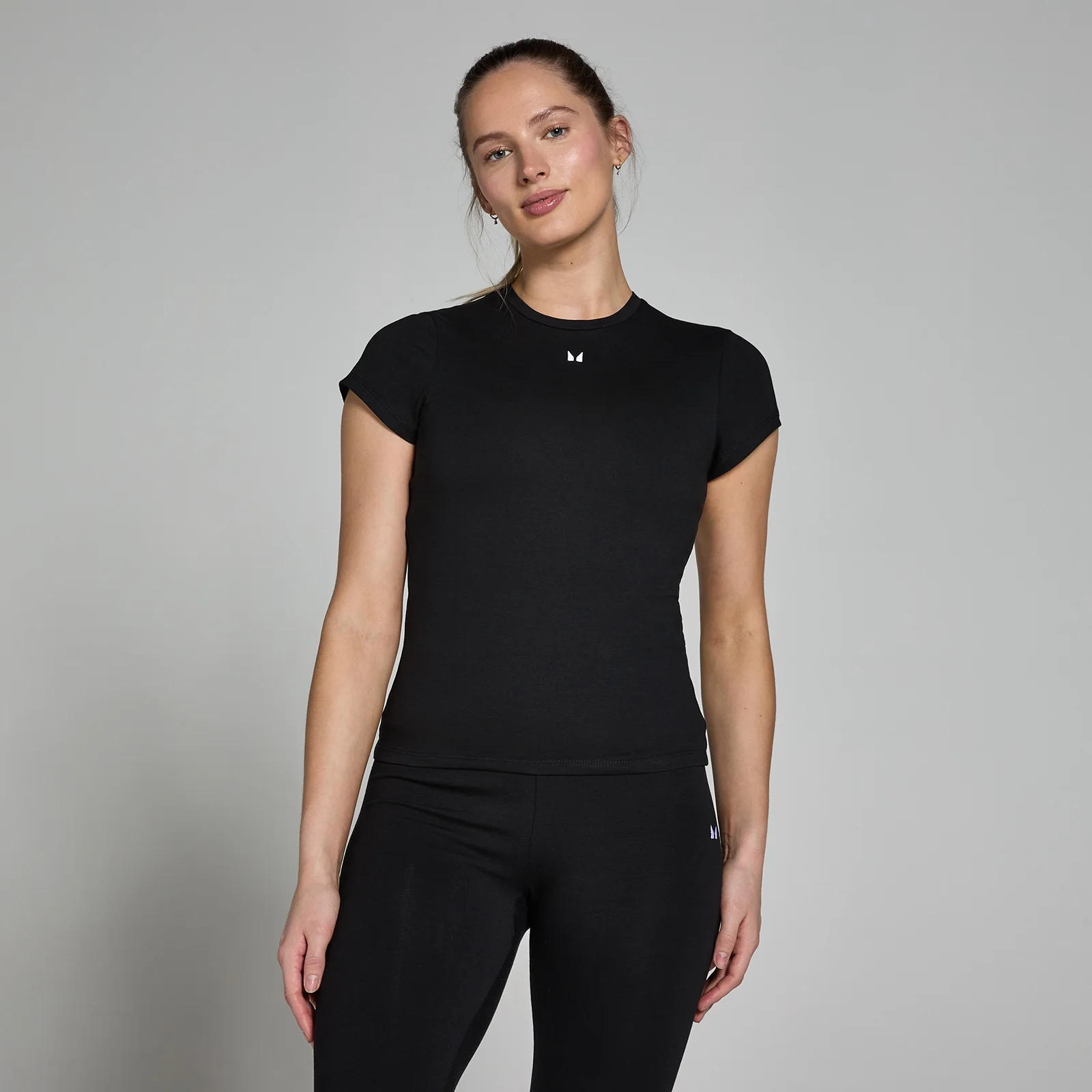 Een vrouw draagt een zwart, nauwsluitend T-shirt met korte mouwen en een klein logo.