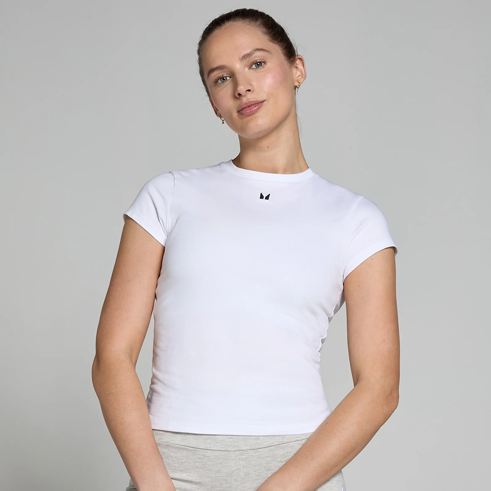 Een vrouw draagt een wit, nauwsluitend T-shirt met korte mouwen en een klein zwart logo.