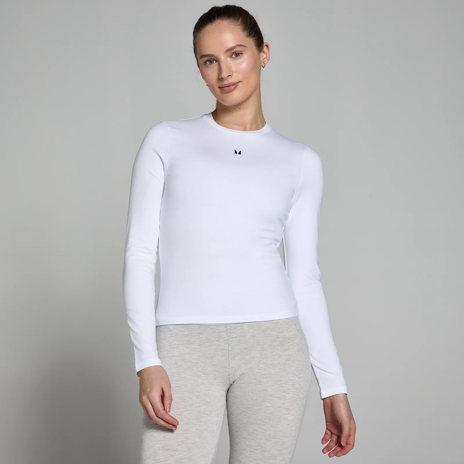 Een vrouw draagt een wit, nauwsluitend T-shirt met lange mouwen en een klein zwart logo.