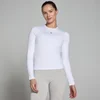 Een vrouw draagt een wit, nauwsluitend T-shirt met lange mouwen en een klein zwart logo.