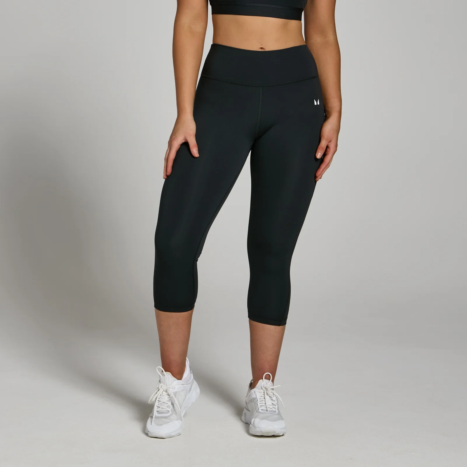 Zwarte, driekwarts sportlegging met hoge tailleband en een klein wit logo op het been.