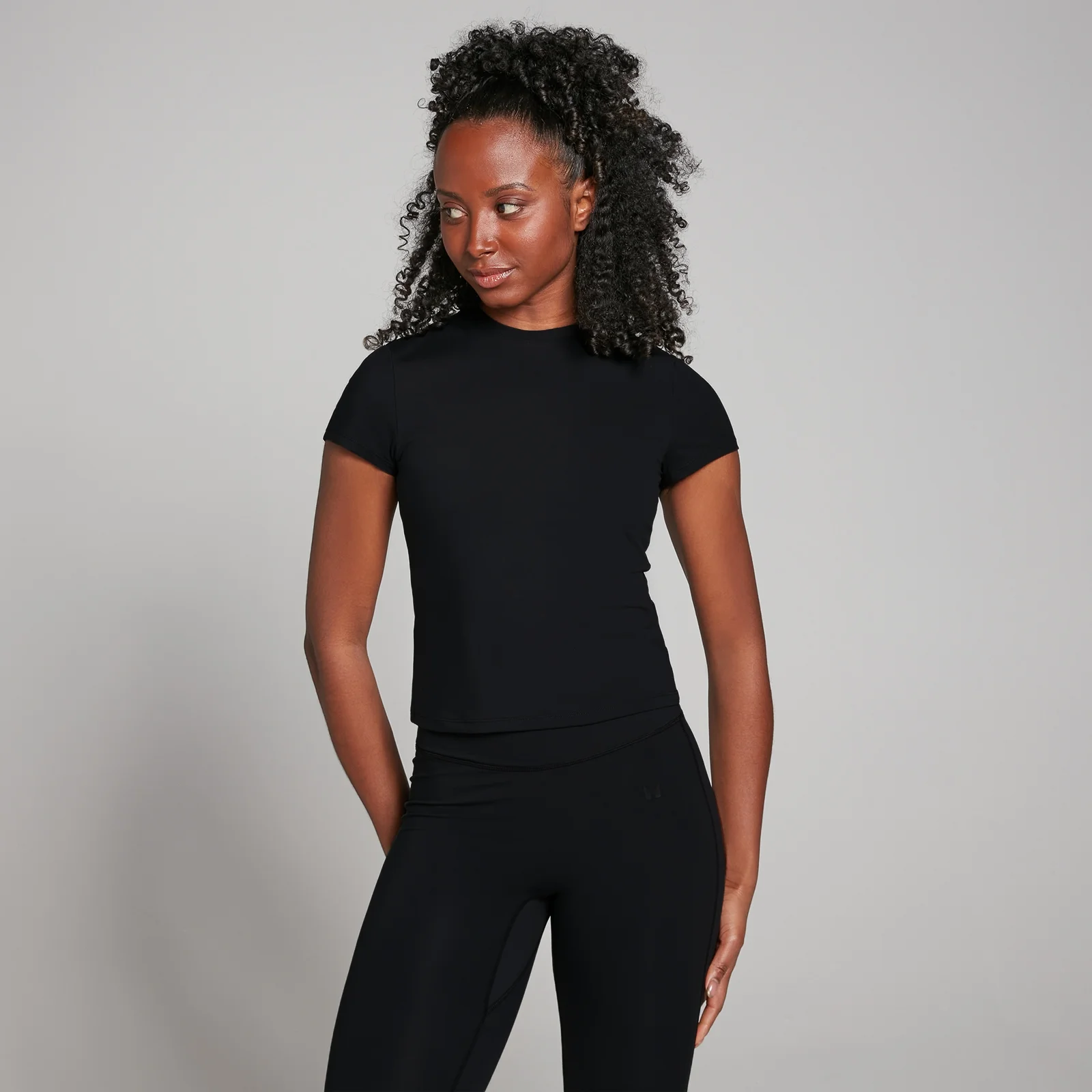 Een vrouw draagt een zwart, nauwsluitend T-shirt met korte mouwen en een zwarte legging.