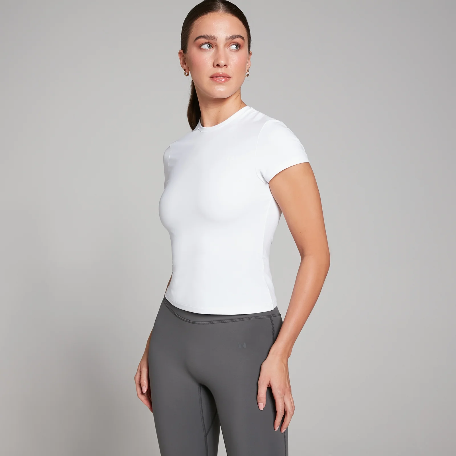 Een witte, nauwsluitende MP T-shirt met korte mouwen, gedragen met grijze leggings.