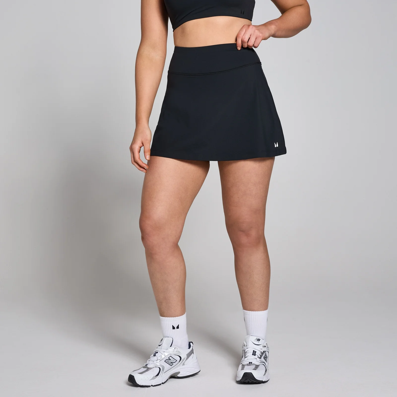 Een zwarte MP dames skort, gedragen met een zwarte sporttop en witte sokken met sportschoenen.