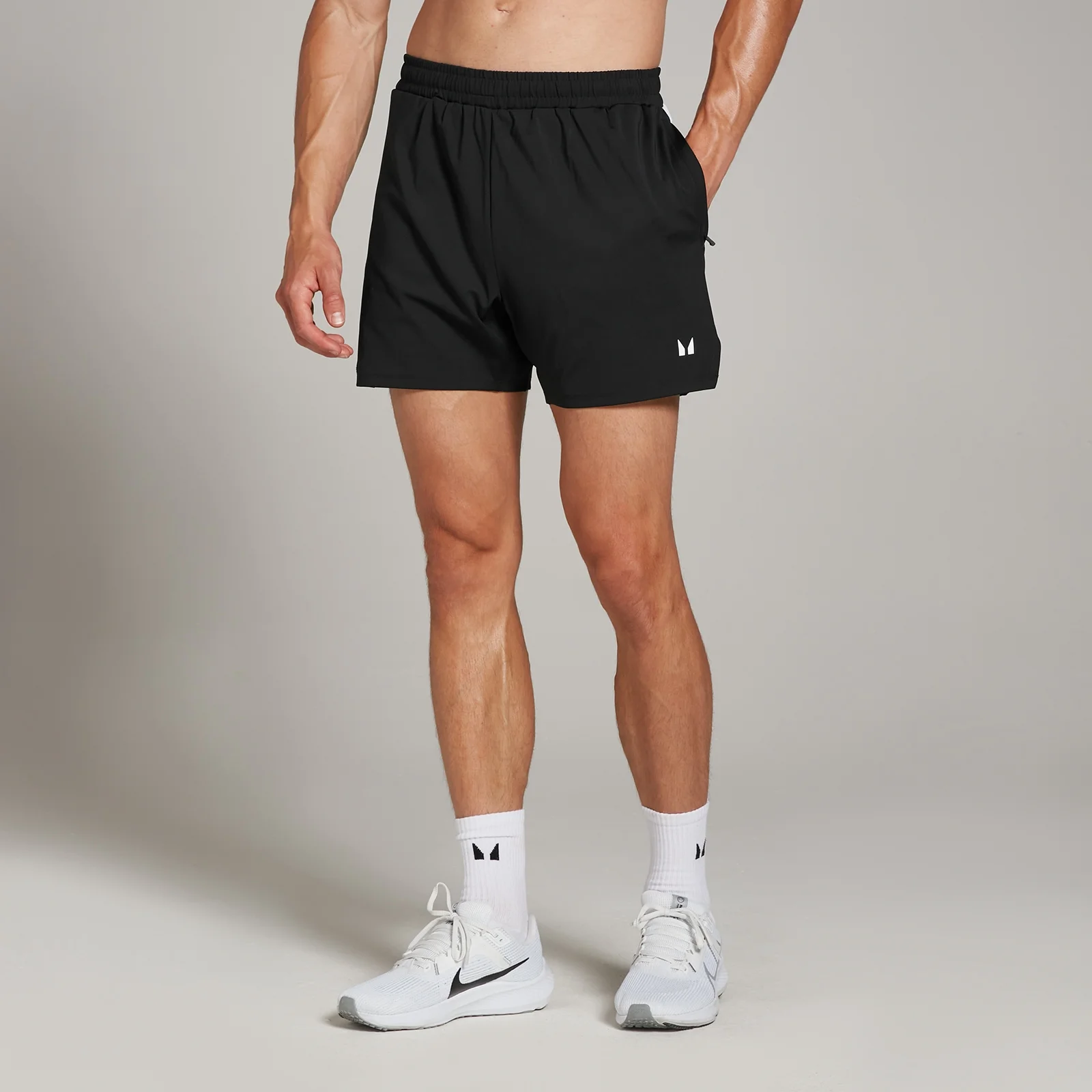 Een man draagt een zwarte MP sportshort met een wit logo, witte sokken en witte sportschoenen.