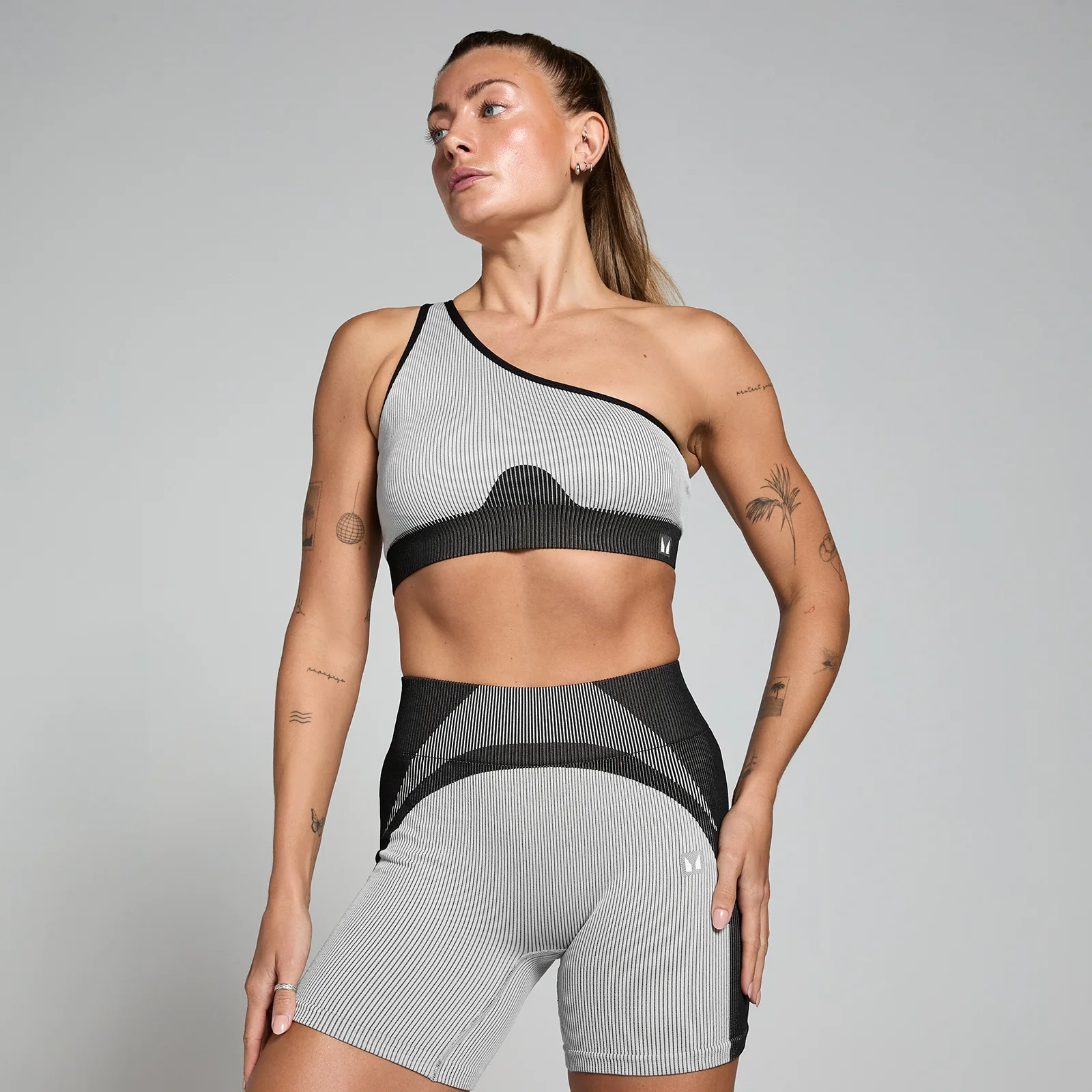 Een vrouw draagt een gestreepte, ribgebreide sportbeha met één schouderband en bijpassende korte broek.