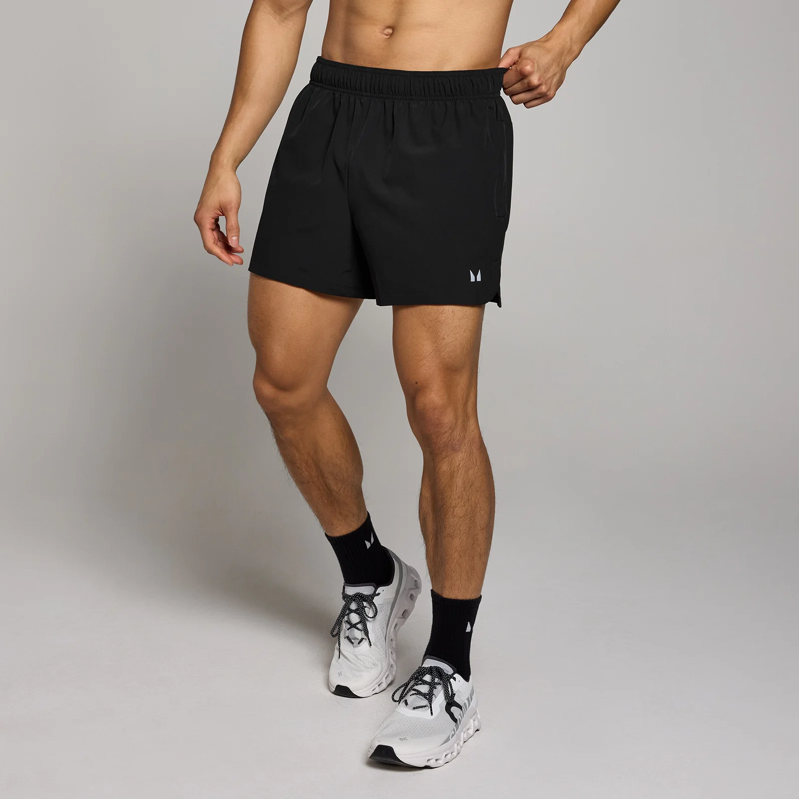 Een man draagt een zwarte, korte sportbroek met een elastische band en witte sportschoenen.