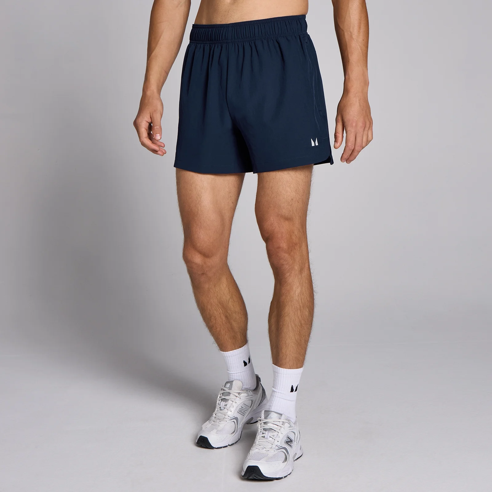 Een man draagt marineblauwe, korte sportbroeken met een elastische tailleband en witte sokken met sportschoenen.